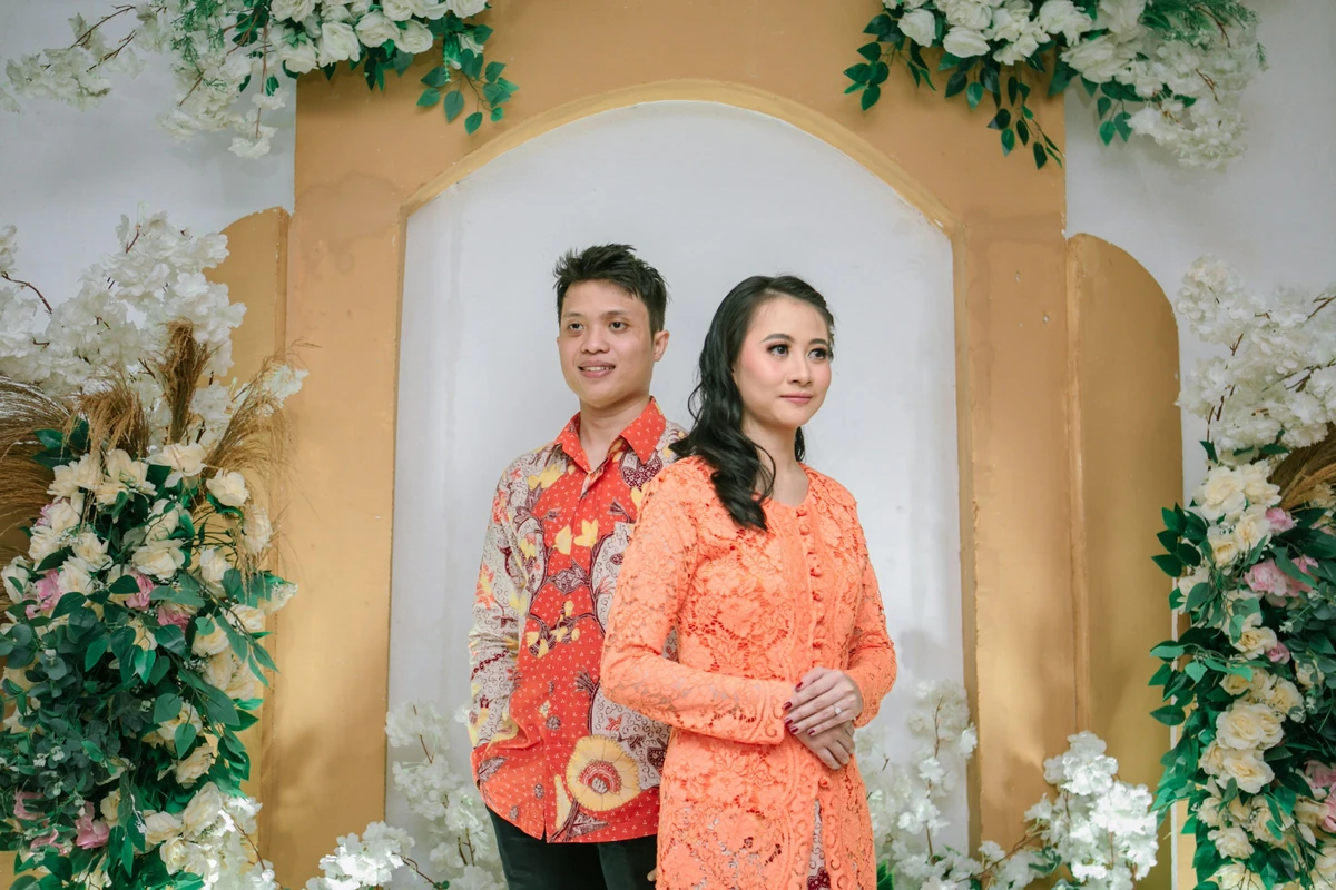 Pasangan berpose di depan pelaminan bunga; foto stok
