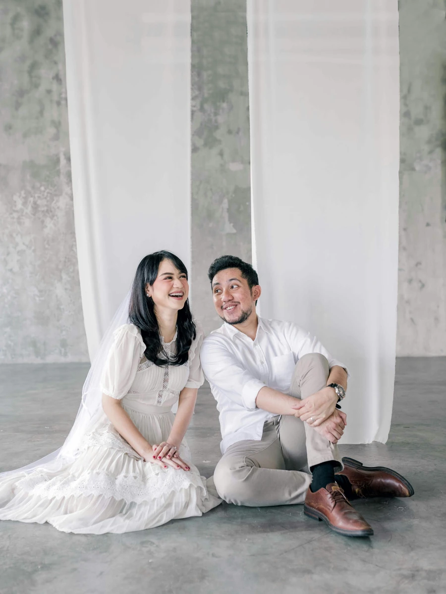 Pasangan duduk tersenyum dalam busana putih; foto stok